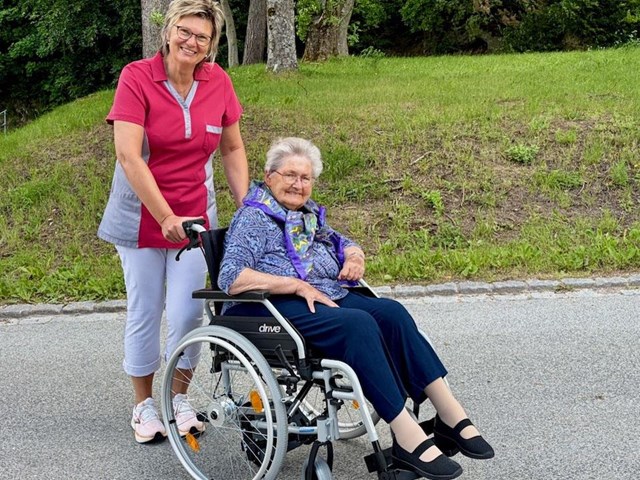 Pflegerin schiebt Frau in Rollstuhl